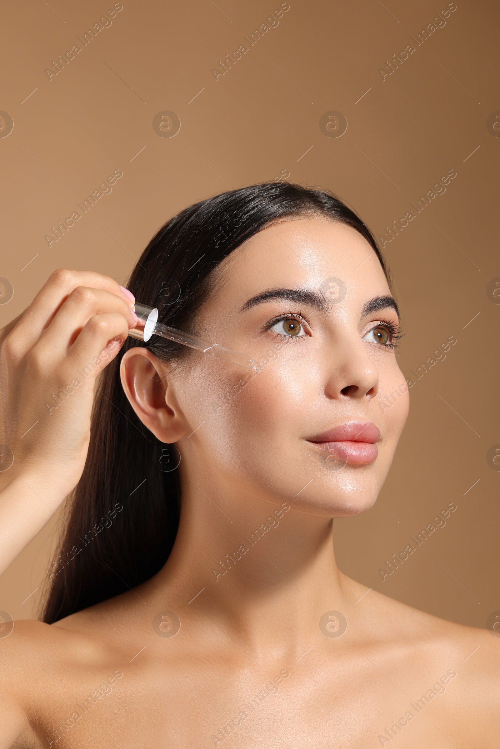 Photo of Beautiful young woman applying serum onto her face on beige background