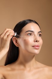 Beautiful young woman applying serum onto her face on beige background