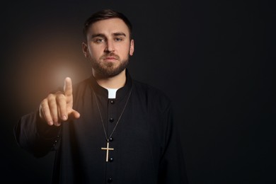 Image of Priest wearing cassock with clerical collar on black background. Space for text