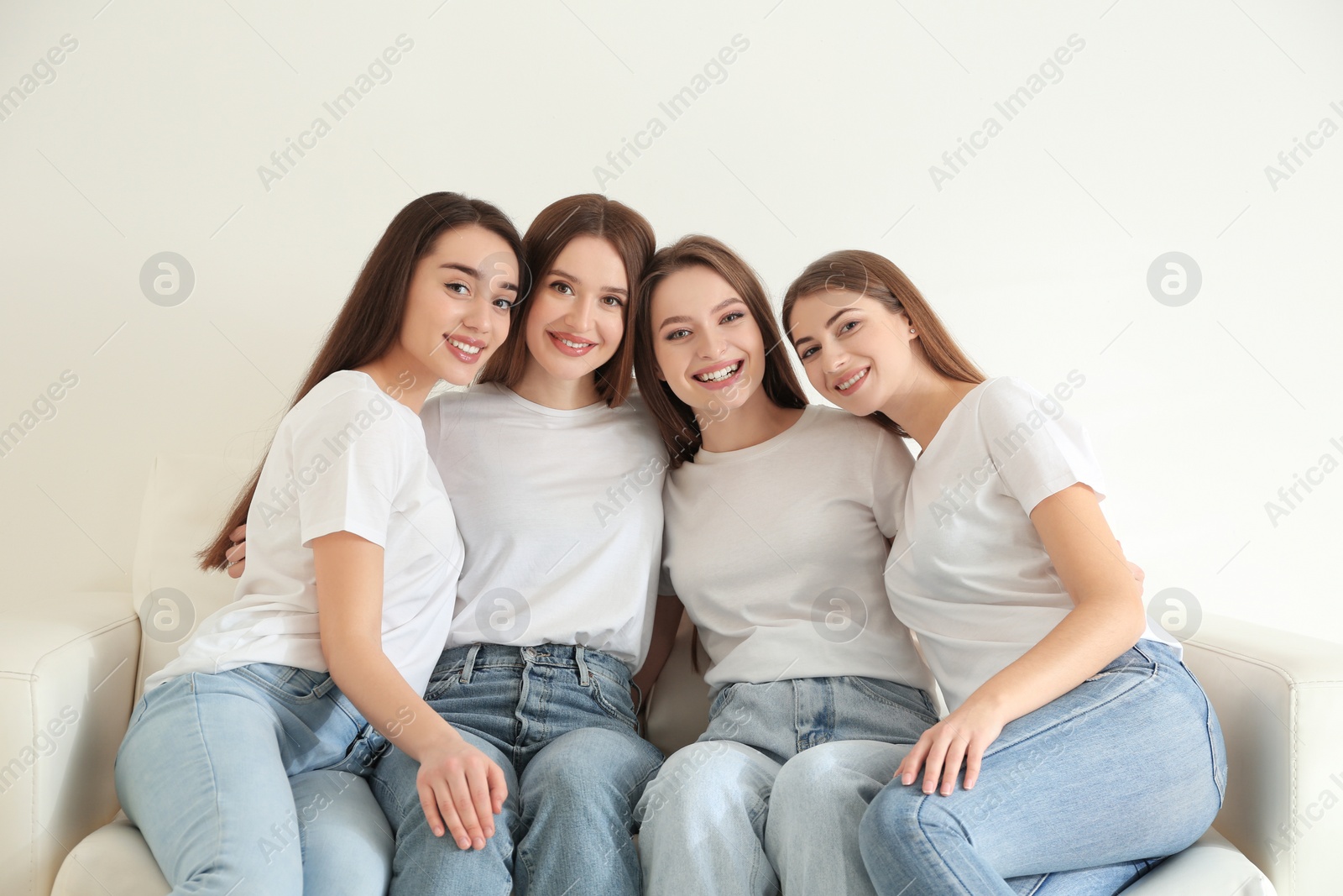 Photo of Beautiful young ladies in jeans and white t-shirts on sofa indoors. Woman's Day