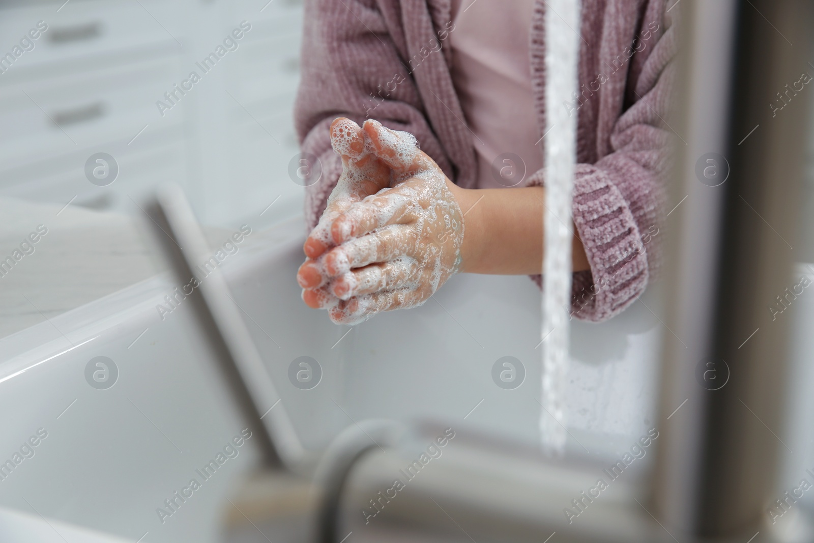 Photo of Little girl washing hands with liquid soap at home, closeup