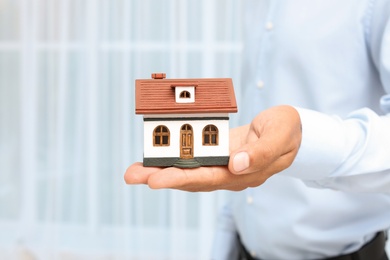 Real estate agent holding house model on blurred background