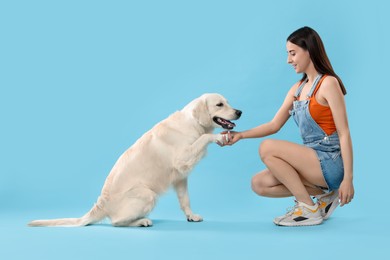 Photo of Cute Labrador Retriever dog giving paw to woman on light blue background. Adorable pet