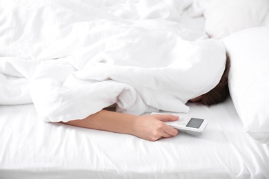 Photo of Woman holding air conditioner remote control in bed, focus on hand
