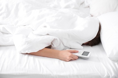 Woman holding air conditioner remote control in bed, focus on hand