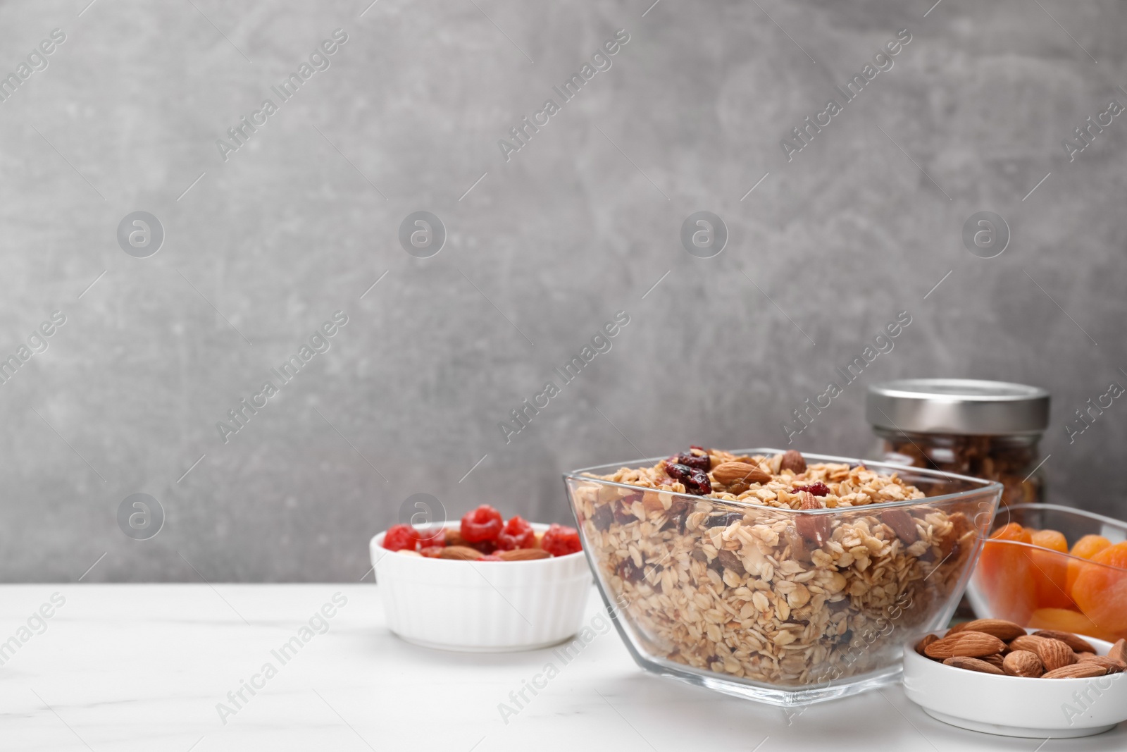 Photo of Tasty granola with nuts and dry fruits on white marble table. Space for text