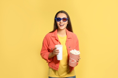 Photo of Woman with 3D glasses, popcorn and beverage during cinema show on color background