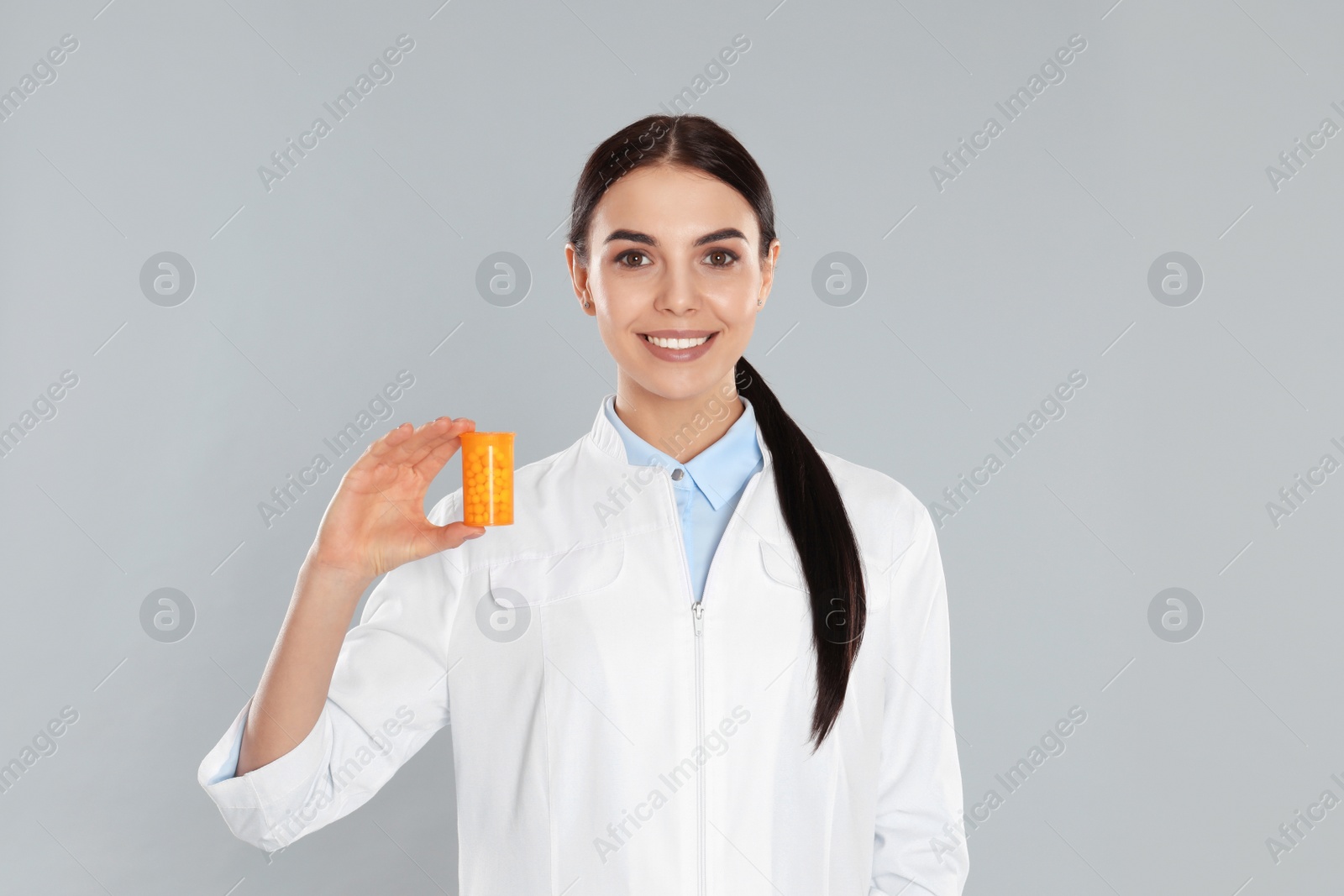 Photo of Professional pharmacist with pills on light grey background