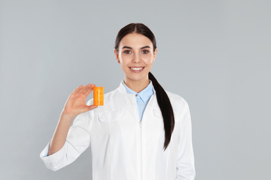 Professional pharmacist with pills on light grey background