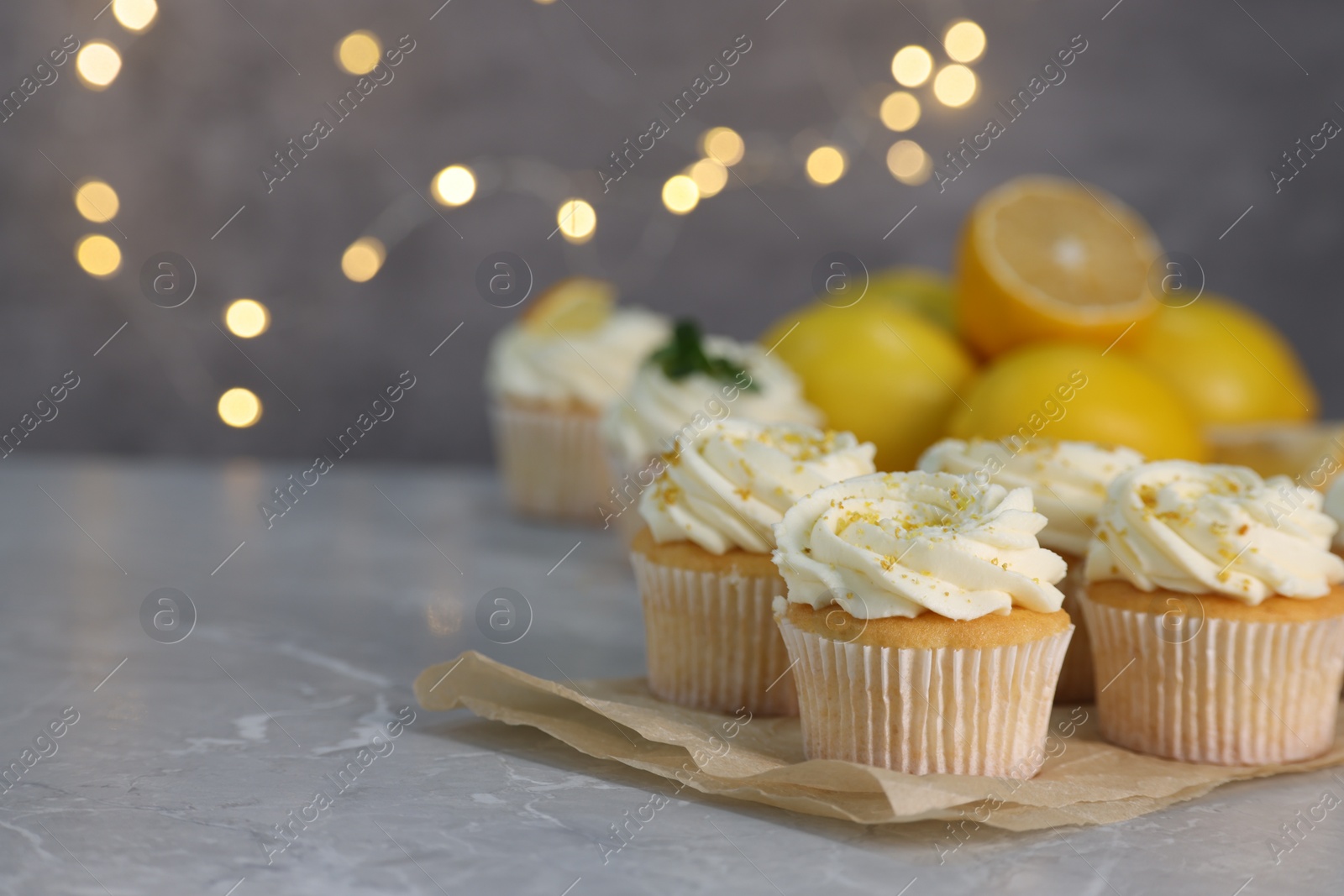 Photo of Delicious cupcakes with white cream and lemon zest on gray marble table, closeup. Space for text
