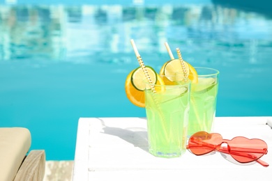 Photo of Refreshing cocktail in glasses and sunglasses near outdoor swimming pool on sunny day. Space for text