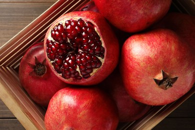 Ripe pomegranates in crate on wooden table, top view
