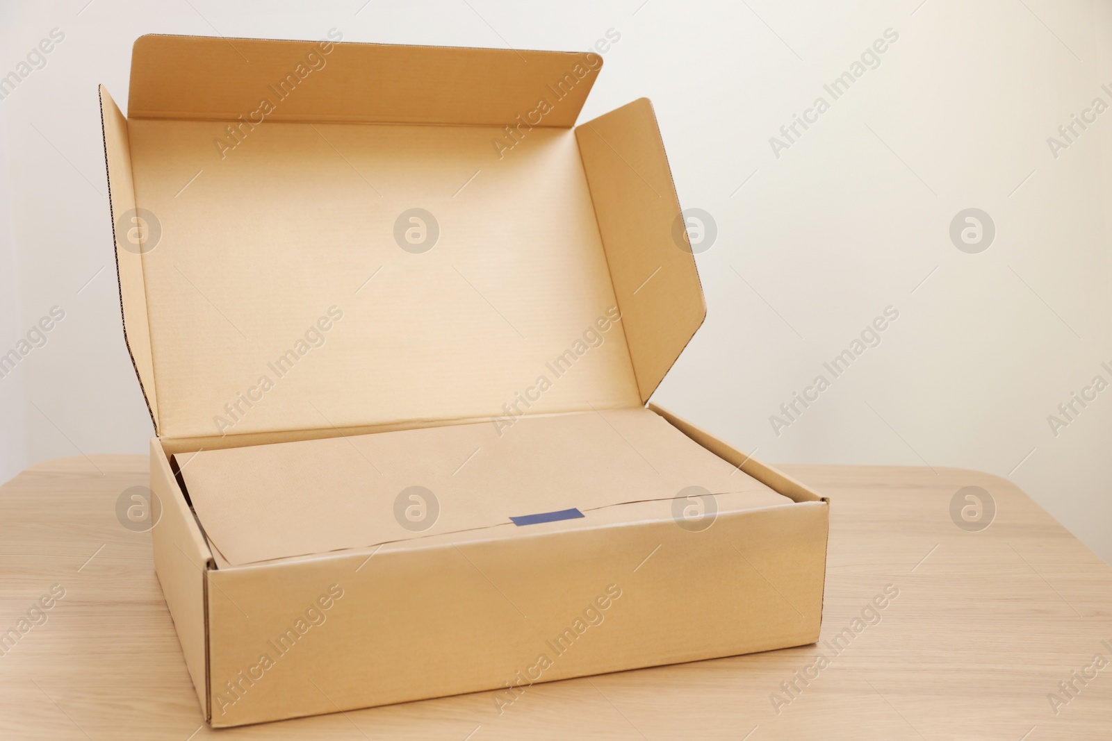 Photo of Open cardboard box with item wrapped in kraft paper on wooden table. Delivery service