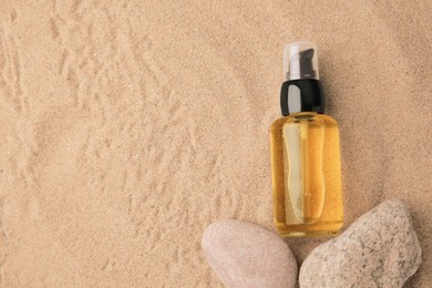 Photo of Bottle of serum and stones on sand, flat lay. Space for text