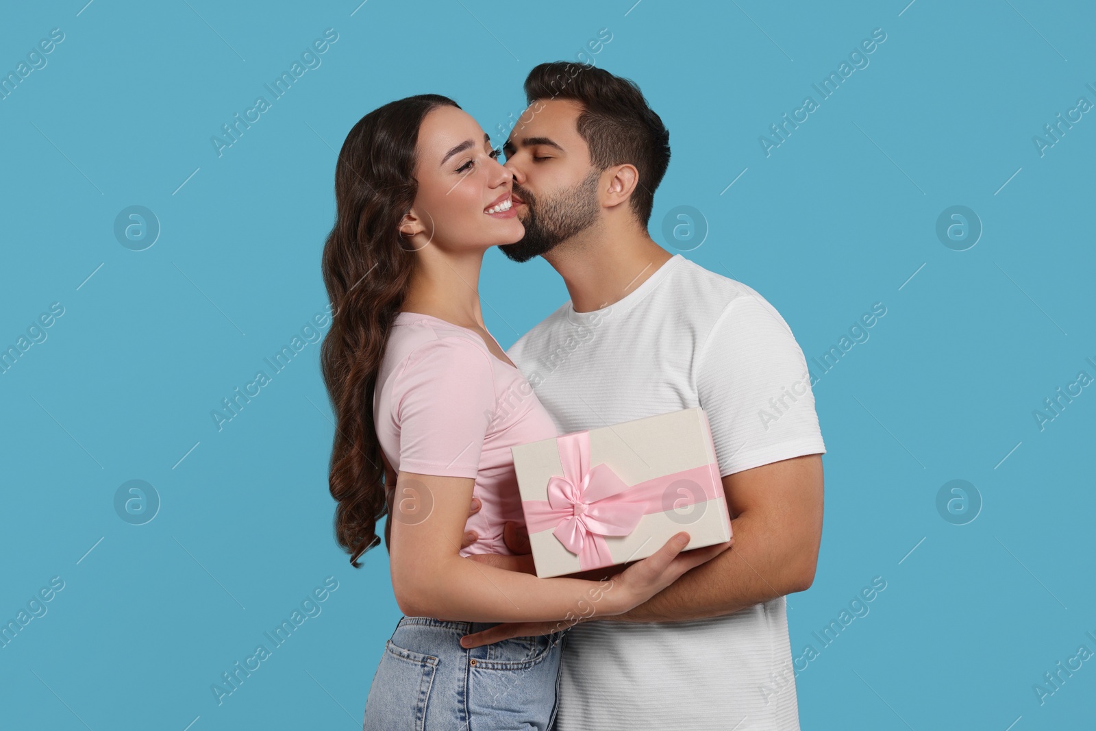 Photo of Man kissing his smiling girlfriend on light blue background. Celebrating holiday