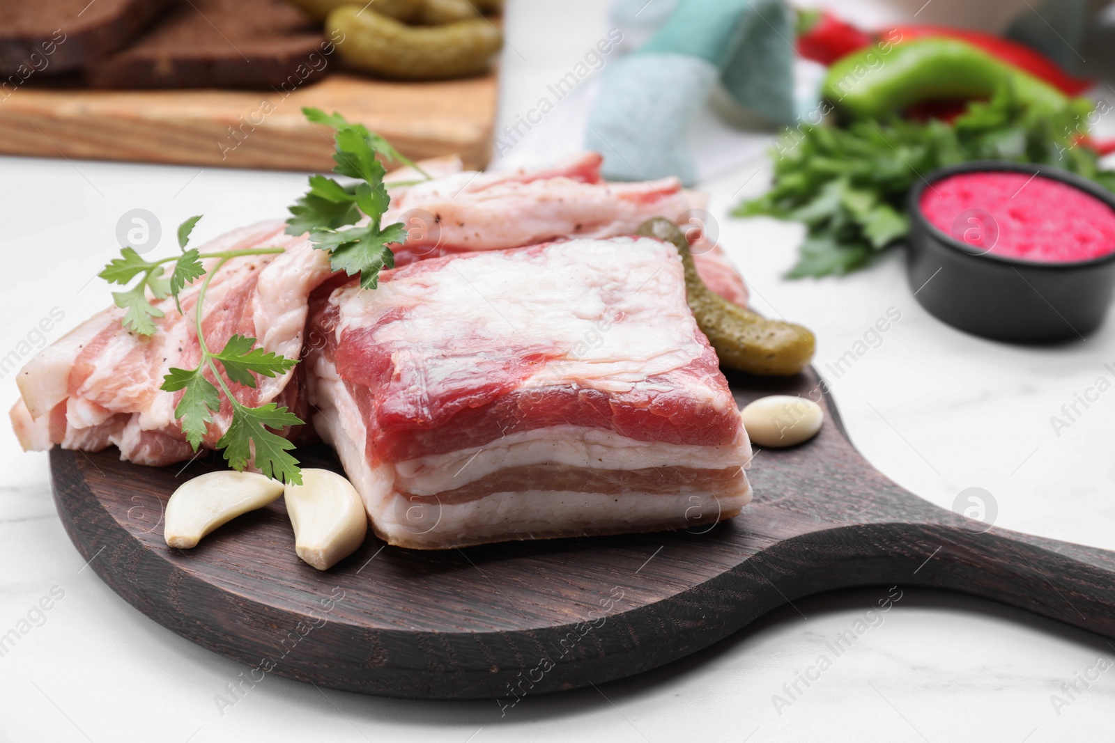 Photo of Tasty pork fatback with pickled cucumber, garlic and parsley on white table, closeup