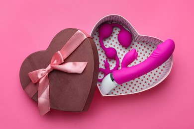 Photo of Gift box with sex toys on pink background, top view