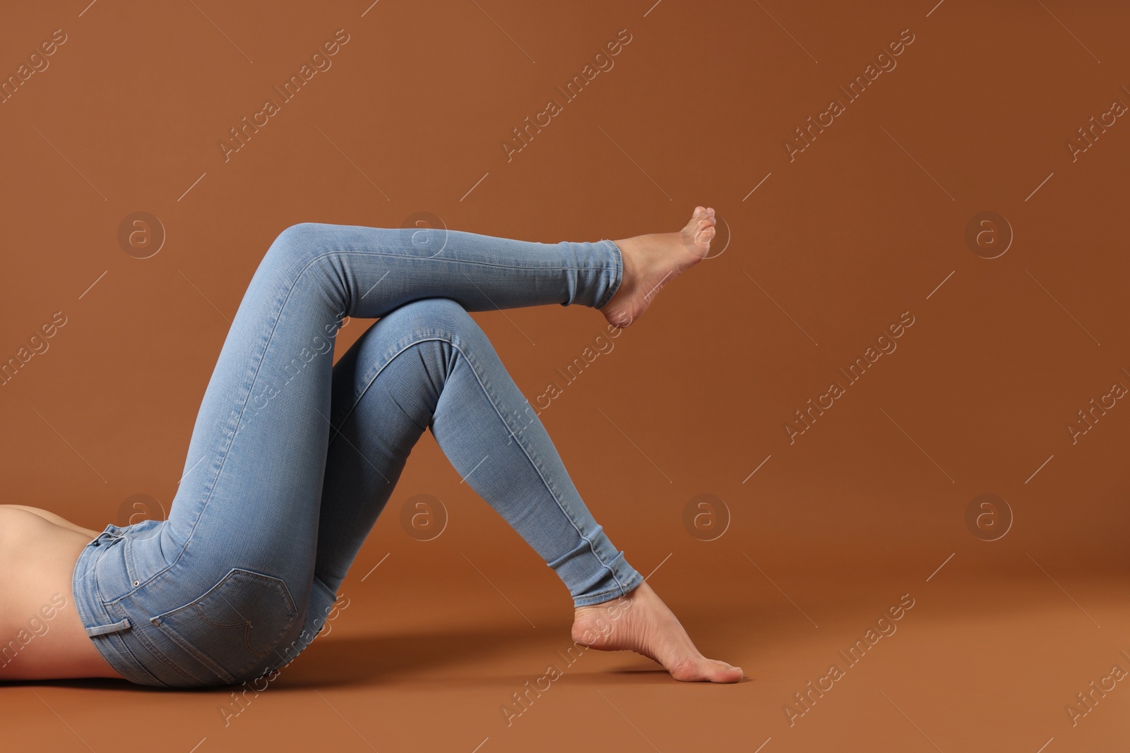 Photo of Woman wearing stylish light blue jeans on brown background, closeup. Space for text