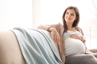 Photo of Young pregnant woman sitting on couch in living room