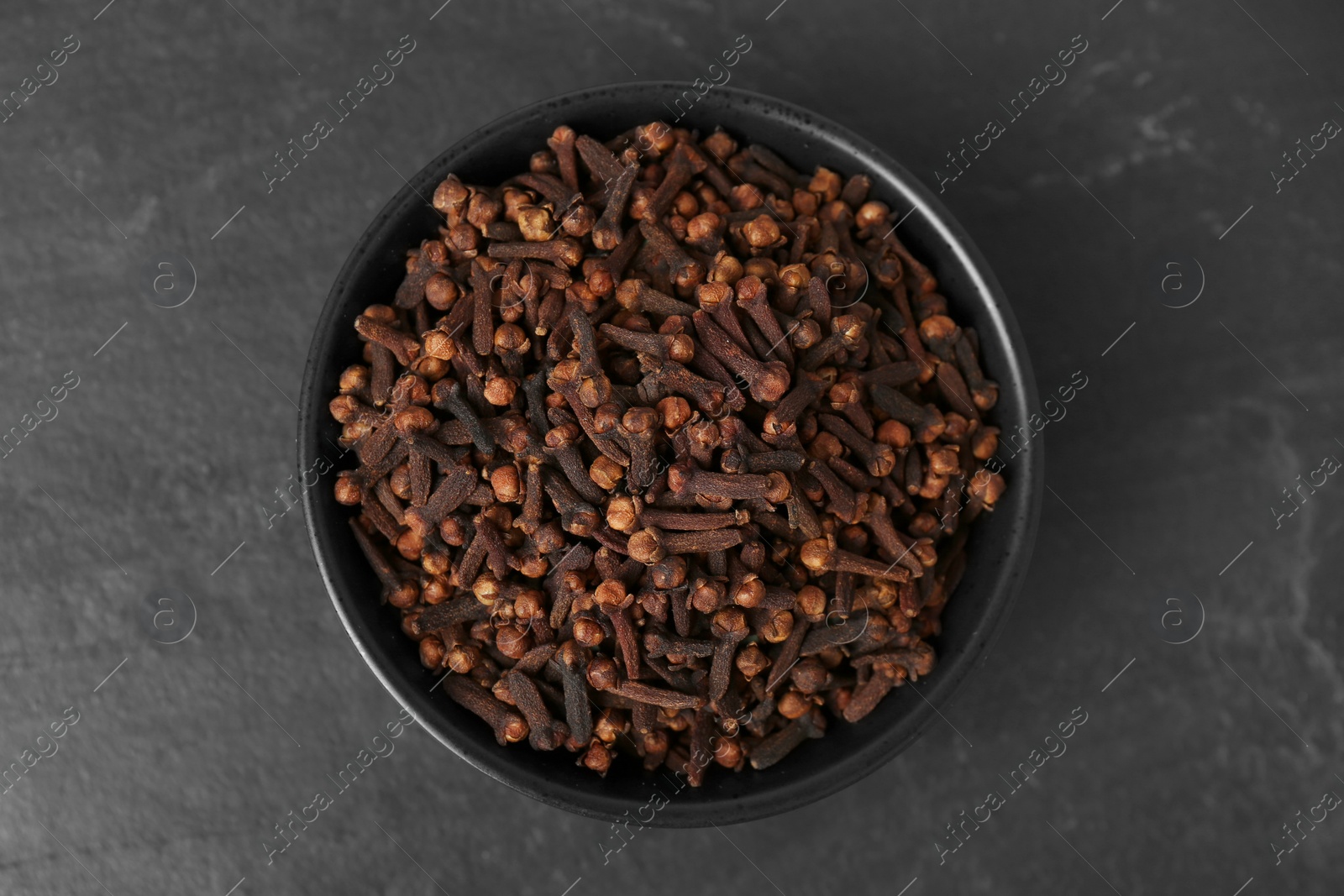 Photo of Bowl of aromatic dry cloves on black table, top view