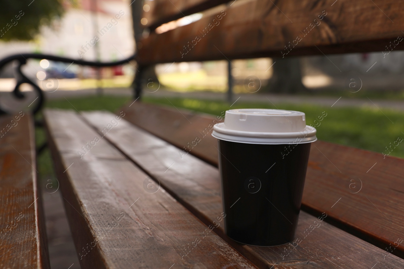 Photo of Takeaway paper cup with plastic lid on wooden bench outdoors, space for text