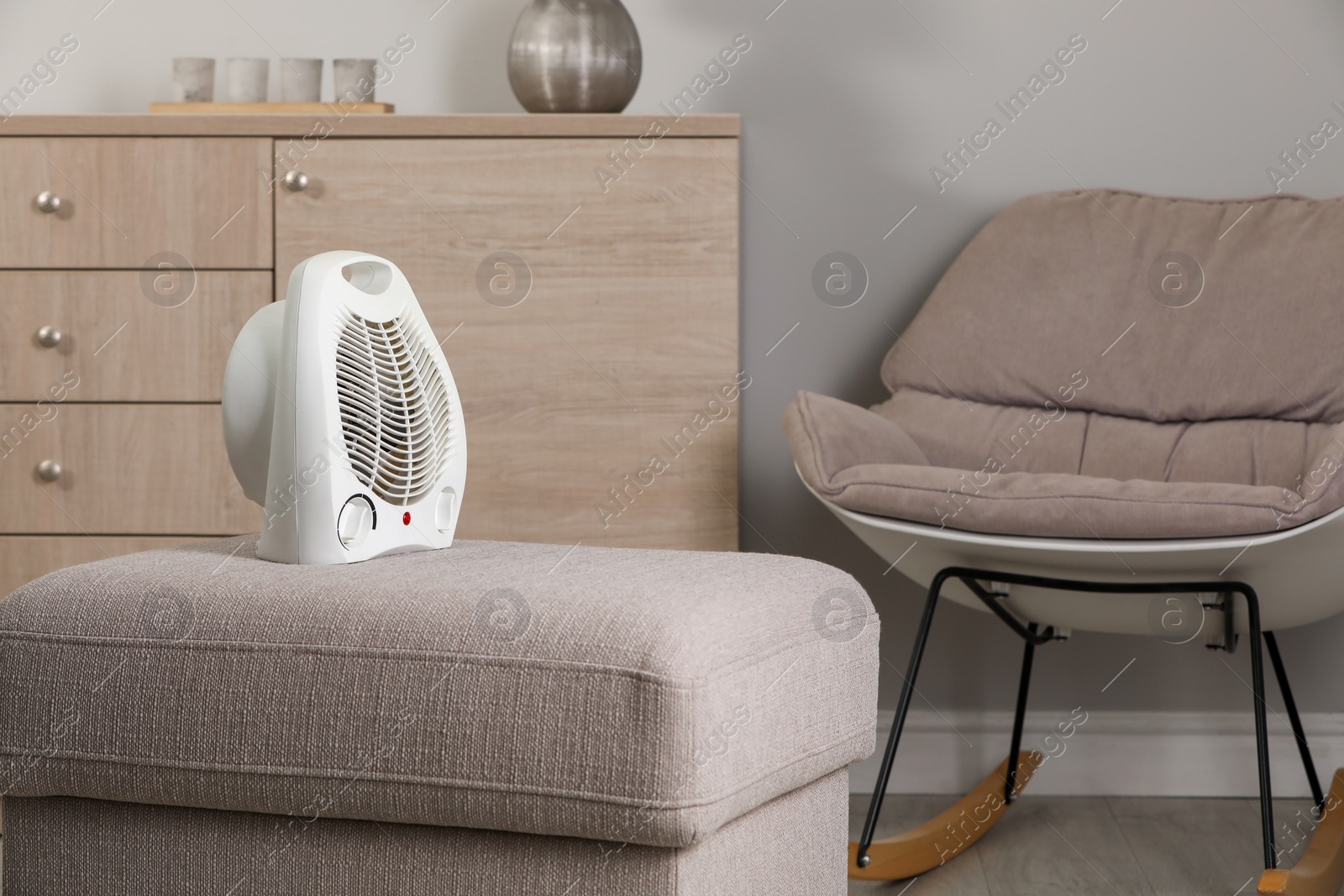 Photo of Modern electric fan heater on pouf in cozy room