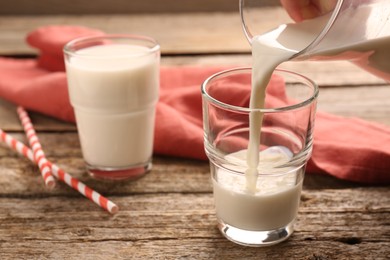 Photo of Pouring tasty milk into glass on wooden table, closeup