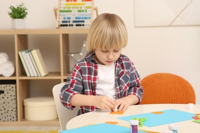 Cute little boy using glue stick at desk in room. Home workplace