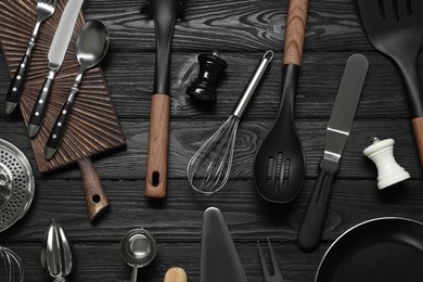 Photo of Set of different kitchen utensils on black wooden table, flat lay
