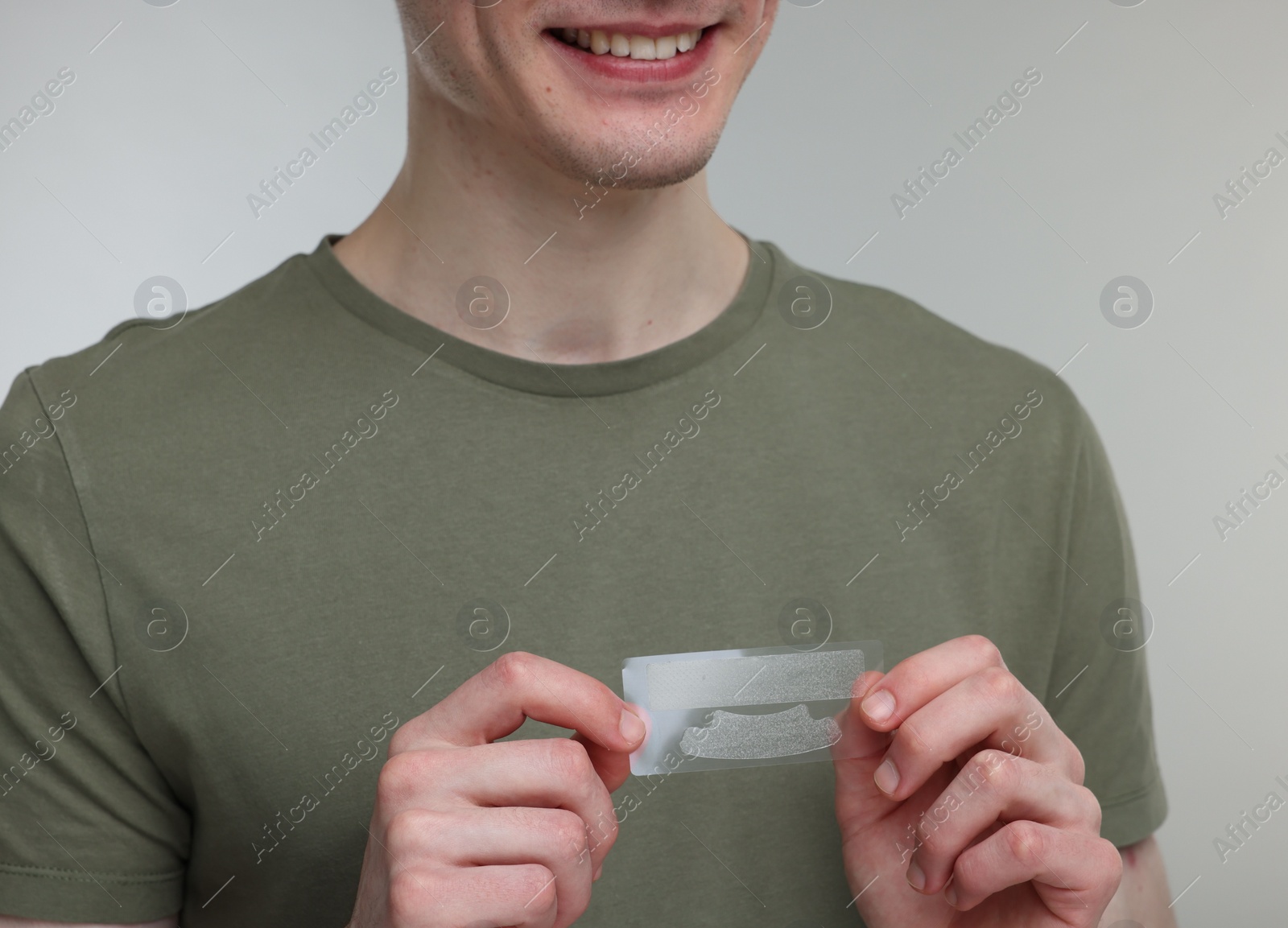 Photo of Young man with whitening strips on light grey background, closeup