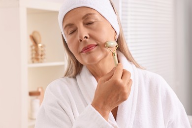 Photo of Woman massaging her face with jade roller in bathroom