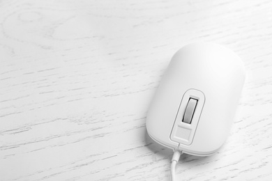 Photo of Modern wired optical mouse on white wooden table. Space for text