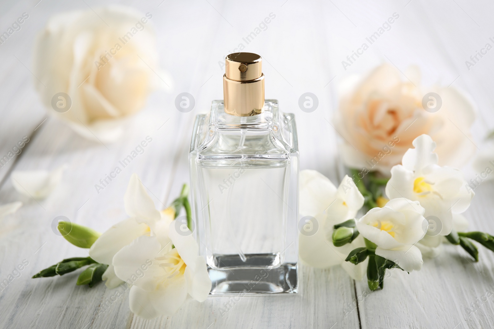 Photo of Bottle of perfume and beautiful flowers on white wooden table
