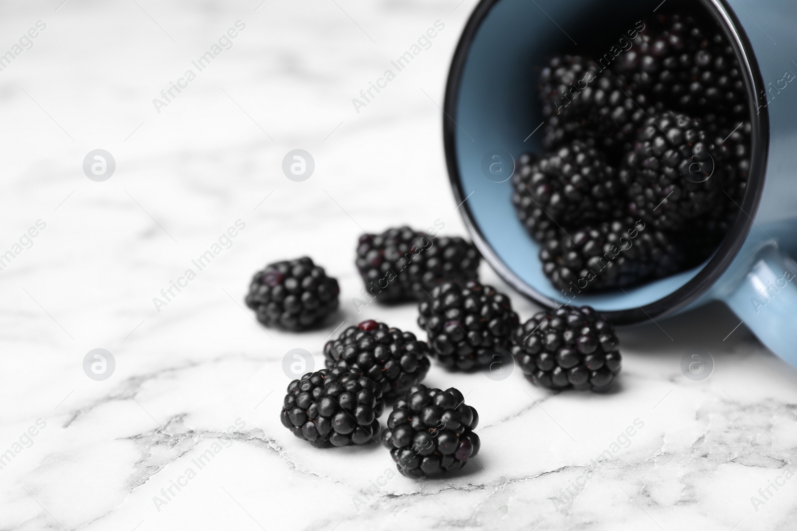 Photo of Overturned mug with blackberries on white marble table, closeup
