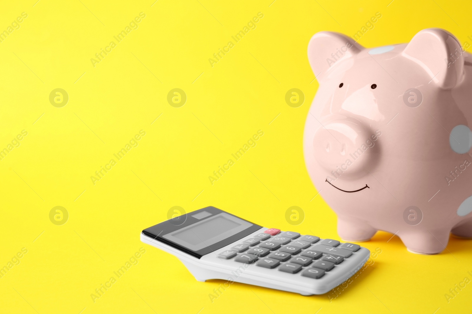 Photo of Calculator and pink piggy bank on yellow background, closeup. Space for text