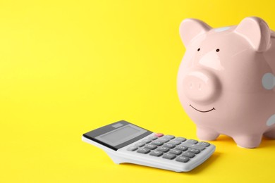 Calculator and pink piggy bank on yellow background, closeup. Space for text