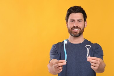 Photo of Happy man with tongue cleaner and plastic toothbrush on yellow background, space for text