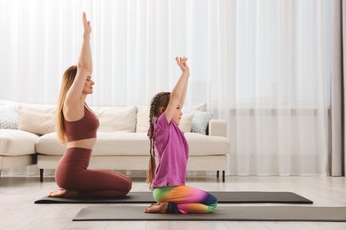 Photo of Mother and daughter in sportswear meditating together at home