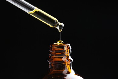 Photo of Dripping tincture from pipette into bottle on black background, closeup