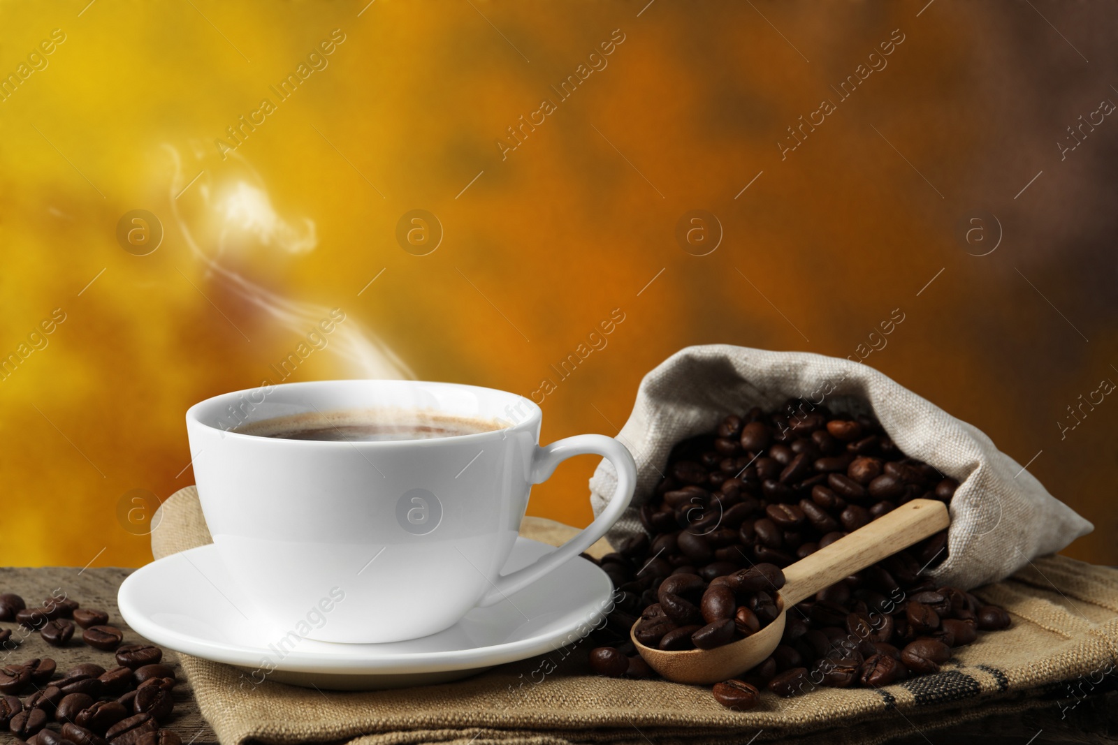 Image of Cup of hot aromatic coffee and roasted beans on wooden table against color background