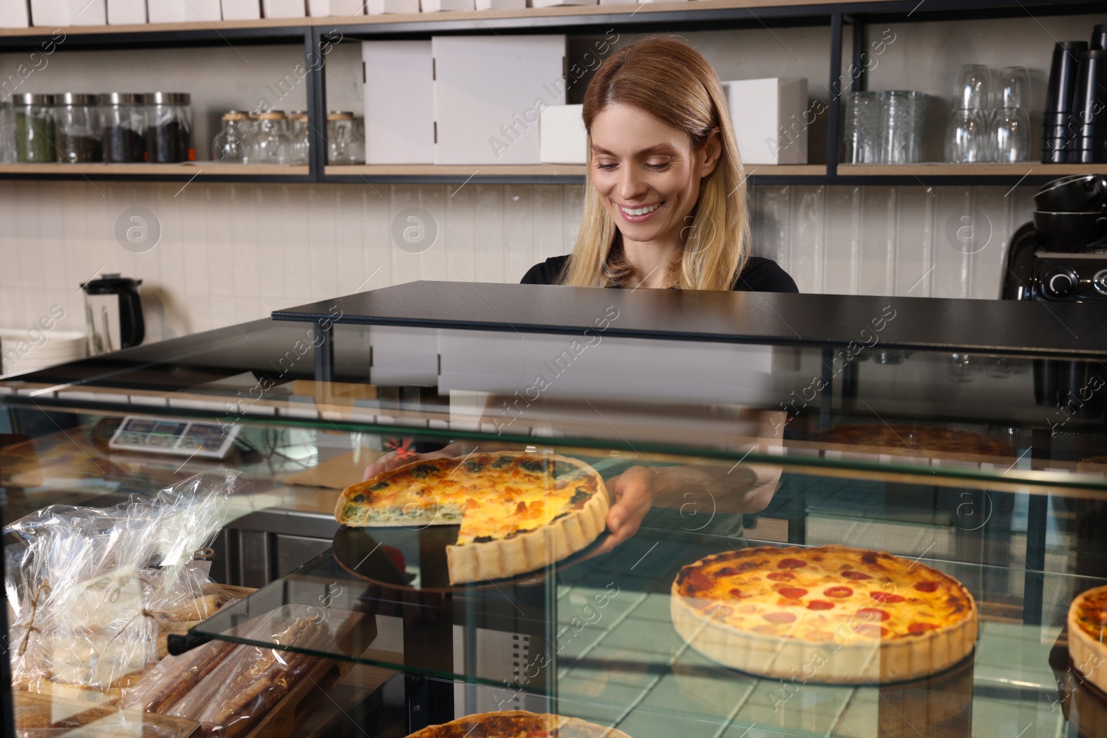 Photo of Happy seller taking delicious quiche from showcase in bakery shop