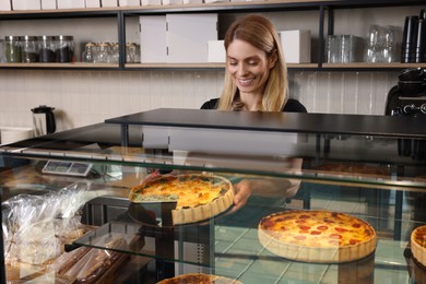 Photo of Happy seller taking delicious quiche from showcase in bakery shop