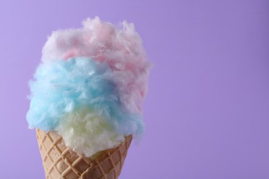 Sweet cotton candy in waffle cone on purple background, closeup. Space for text