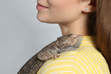 Woman with bearded lizard on grey background, closeup. Exotic pet