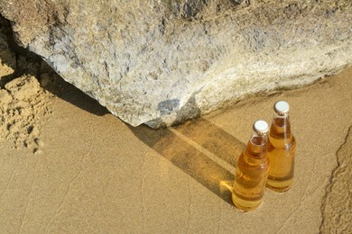 Bottles of cold beer near rock on sandy beach, above view. Space for text
