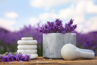 Photo of Spa stones, fresh lavender flowers and white marble mortar on wooden table outdoors, closeup