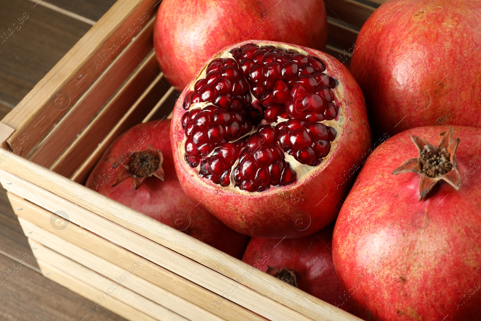 Photo of Ripe pomegranates in wooden crate on table, closeup