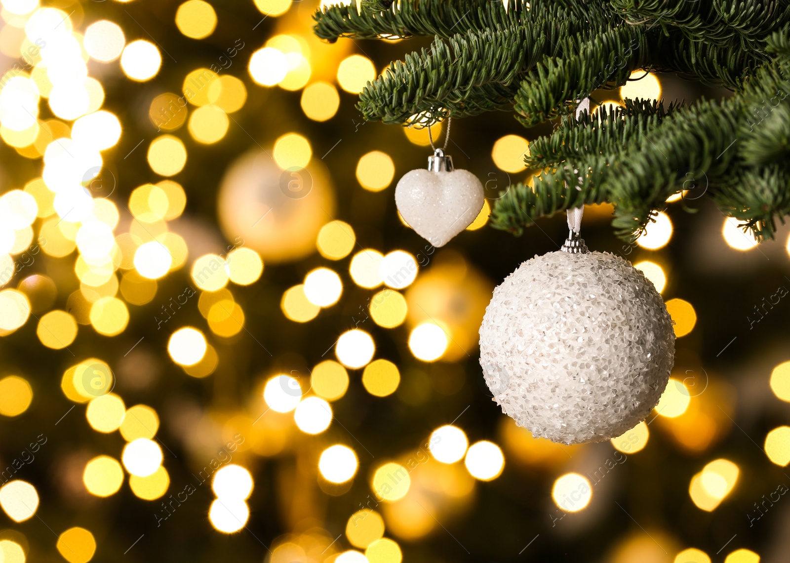 Photo of Beautiful Christmas baubles hanging on fir tree branch against blurred lights, closeup. Space for text