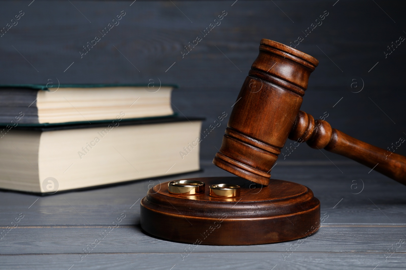 Photo of Divorce concept. Gavel and wedding rings on grey wooden table, space for text