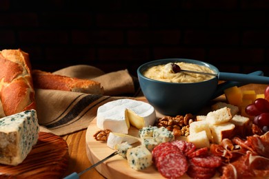 Photo of Fondue pot with tasty melted cheese, forks and different snacks on wooden table